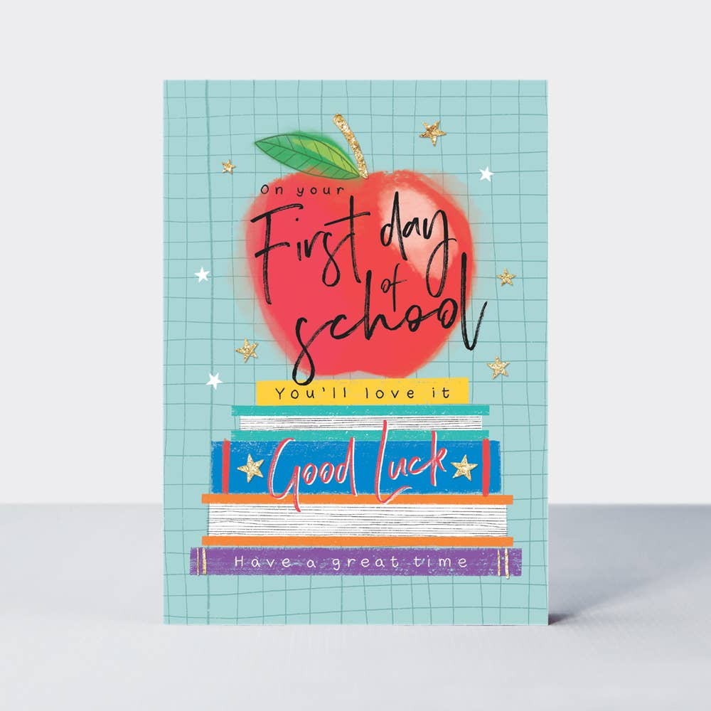 A greeting card with an illustration of an apple and books, titled 'First Day of School' with a wish for good luck.
