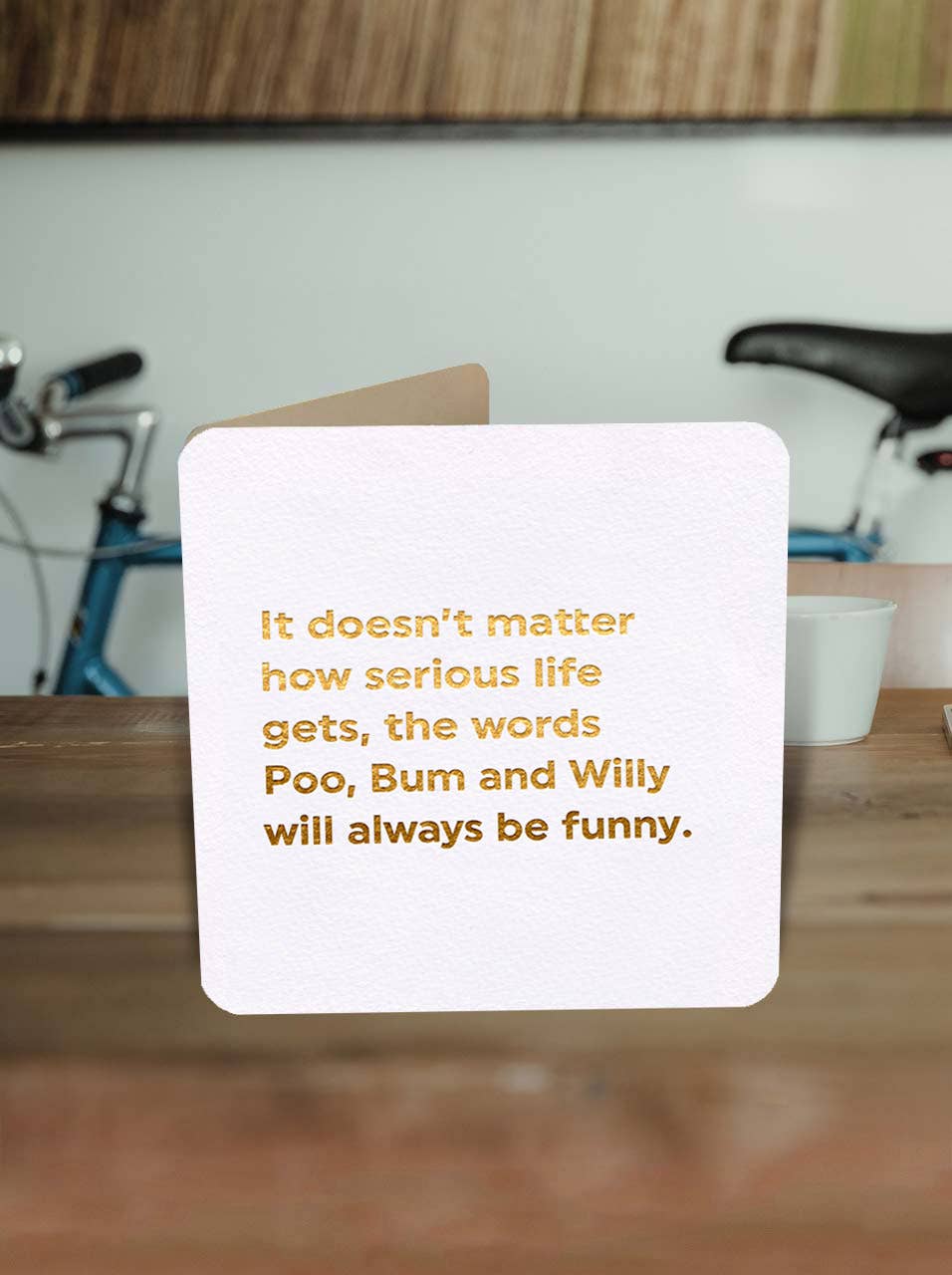 Card with humorous text on a wooden surface with bicycles in the background