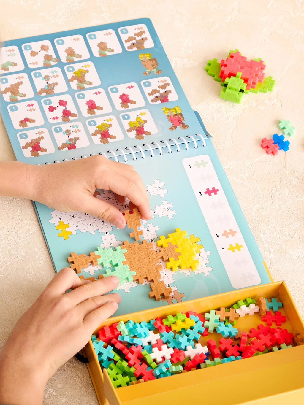 Child playing with a puzzle book and colorful wooden pieces on a light surface.