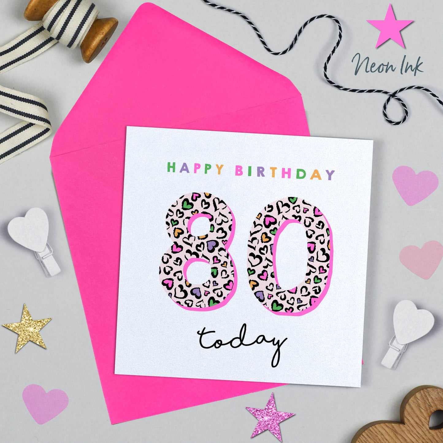 Happy 80th birthday card with pink envelope and decorative items on a light gray background