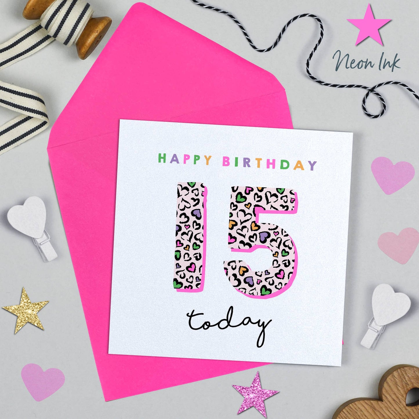 Birthday card with colorful '15' design on a pink envelope with decorative items around.