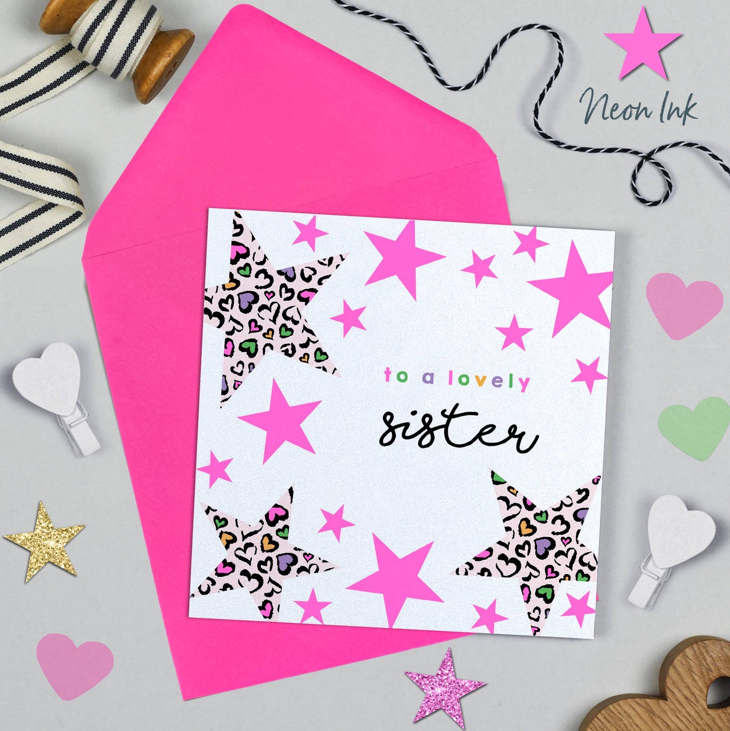 Greeting card with pink stars and leopard print hearts on a pink envelope, surrounded by decorative items.