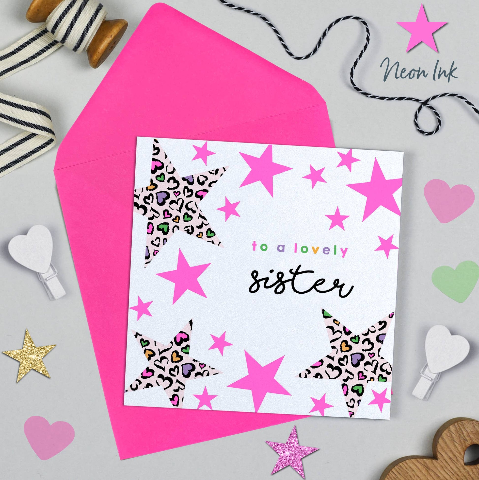 Greeting card with pink stars and leopard print hearts on a pink envelope, surrounded by decorative items.