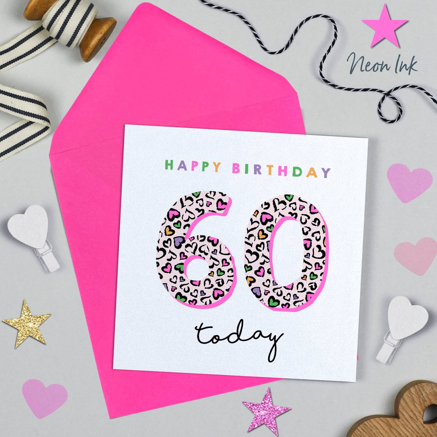 60th birthday card with leopard print numbers on a pink envelope, surrounded by decorative items.