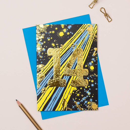 A colorful birthday card with gold foiling, featuring a bold number 14 in the center, placed on a table with a blue envelope and a pencil.