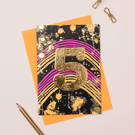 A vibrant birthday card with a gold foiled number 5 on a black background, accompanied by an orange envelope and a pencil on a white surface.