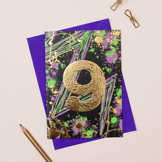 A colorful birthday card with gold foiling, designed for a 9-year-old girl, placed on a table with a purple envelope and a pencil.
