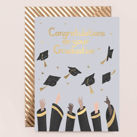 A graduation-themed greeting card with caps and hands in the air, accompanied by a striped Kraft envelope.