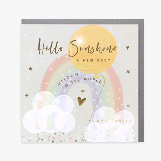 A greeting card with 'Hello Sunshine' text, a rainbow, stars, and a gold-colored sun above a depiction of a newborn. The card has a blank inside and includes a silver envelope.