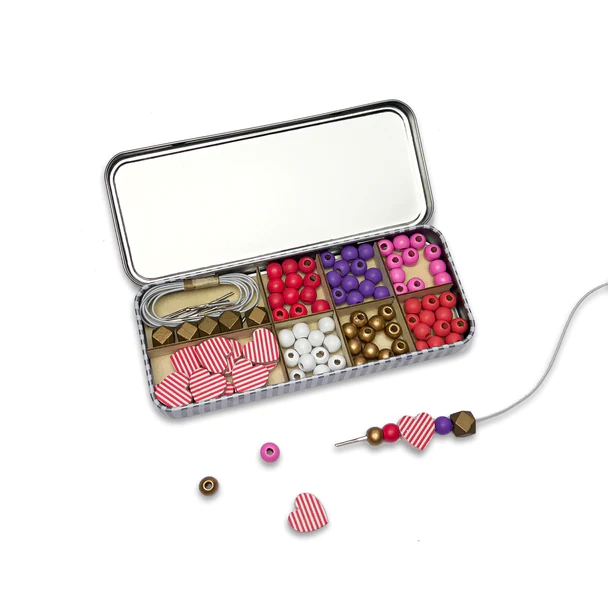 A white background with an open tin of heart beads and other smaller beads.