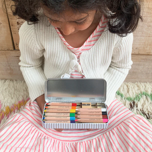 A little girl in a pink striped dress holding an open tin.