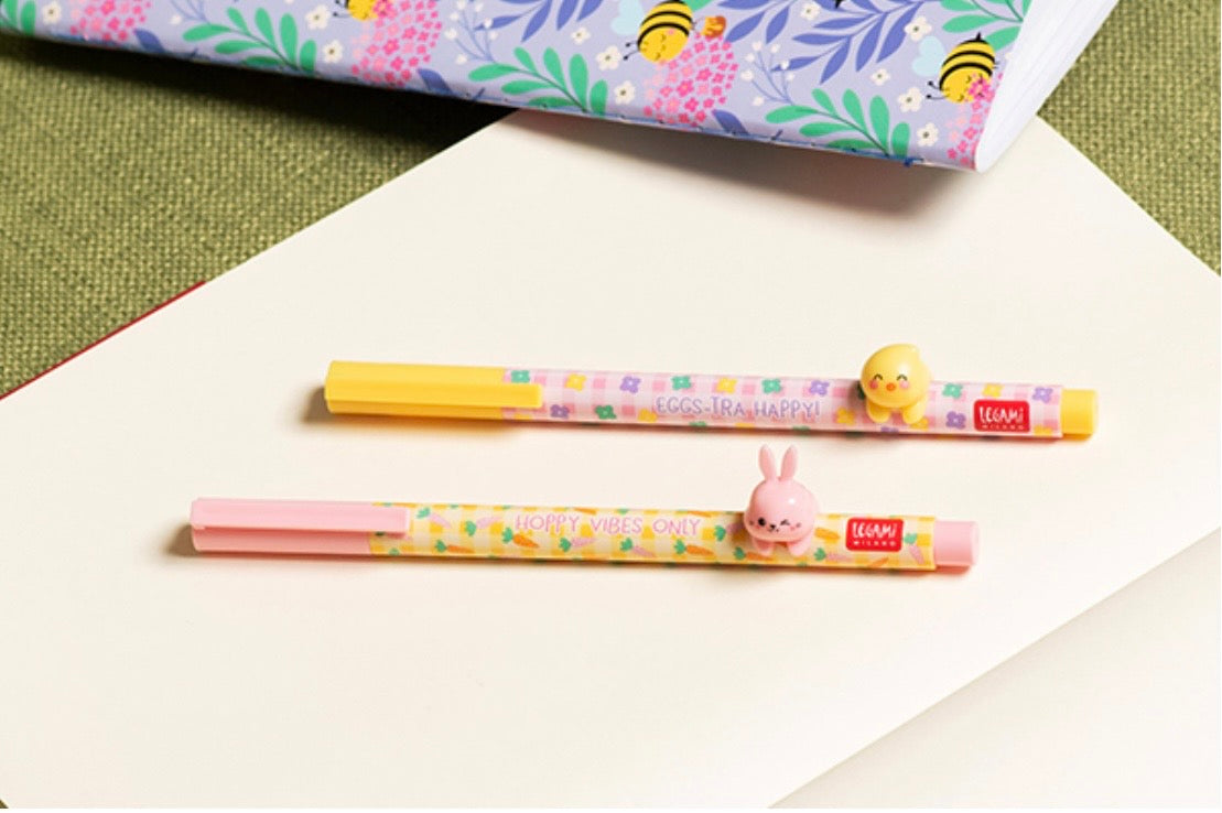 Two cartoon-themed pens on a white surface with a colorful bee-themed paper in the background.