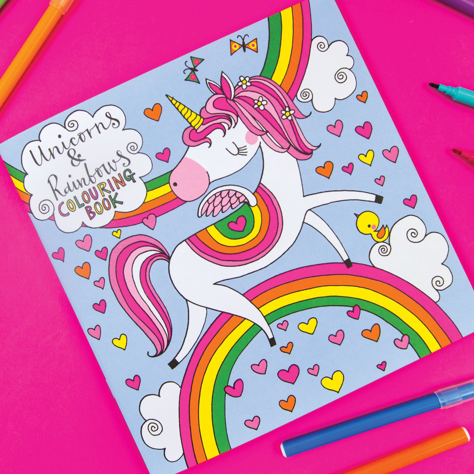 A Colouring Book front cover with a large unicorn and rainbows on a pale blue background and pens around the outside.