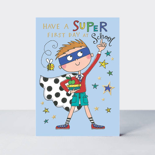 A greeting card featuring a colorful illustration of a cartoon boy in a superhero costume, with a 'First Day at School' text, and gold foil details.