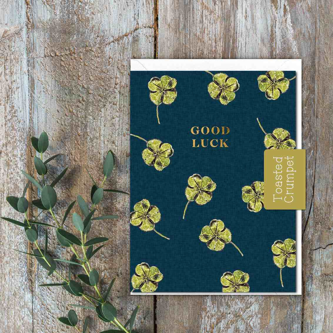 A Dark blue greeting card with four leaf clovers on it and the words Good Luck in gold.