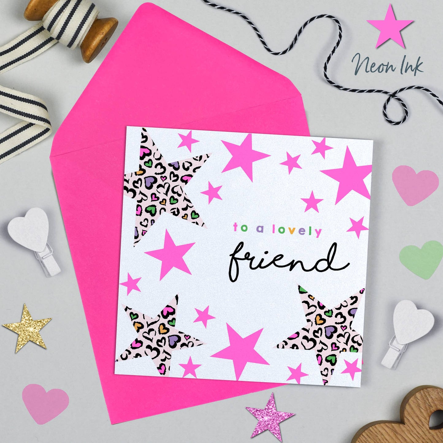Greeting card with pink stars and 'to a lovely friend' text, surrounded by decorative items on a gray background.
