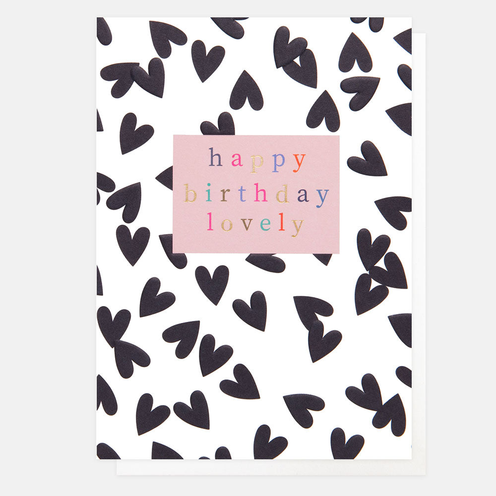 A white card with black hearts on it and the words "Happy Birthday Lovely" in a pink box, with multi-coloured writing in the centre.