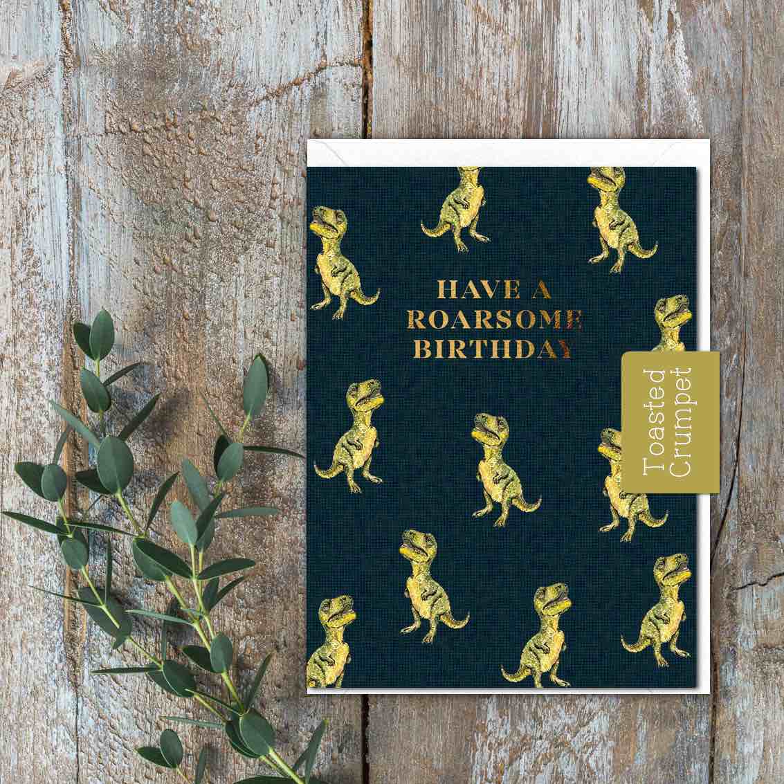 A small black card with green T Rexes and the words Have a roarsome Birthday