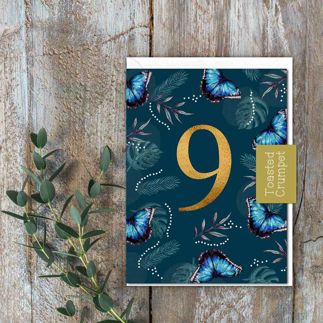 A dark teal card with the number 9 on it along with blue butterflies and flowers.