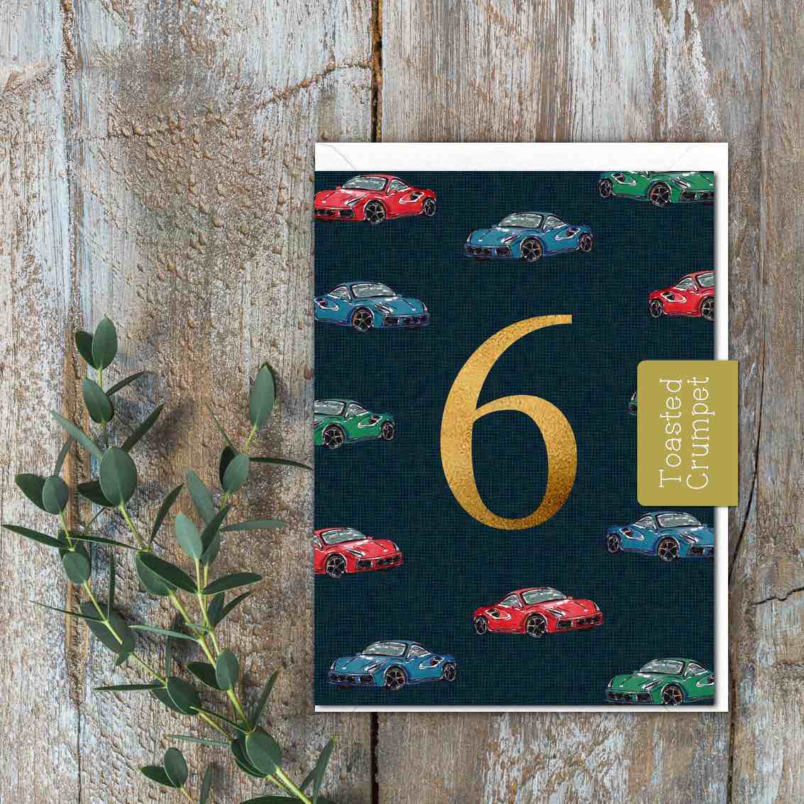 A small card with red, green and blue cars and a large gold 6 in the middle.